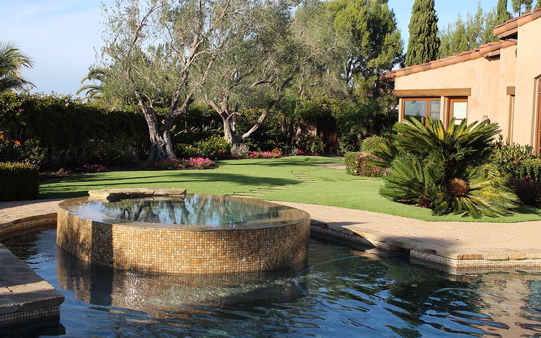 Image of a backyard with a pool and hot tub and artificial grass around the pool area.